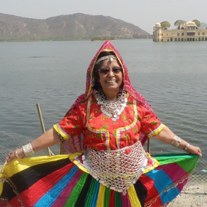 Alijah Saheba Dr. Salimah Punjanistands at the edge of a body of water smiling and showing off a colorful dress and scarf.