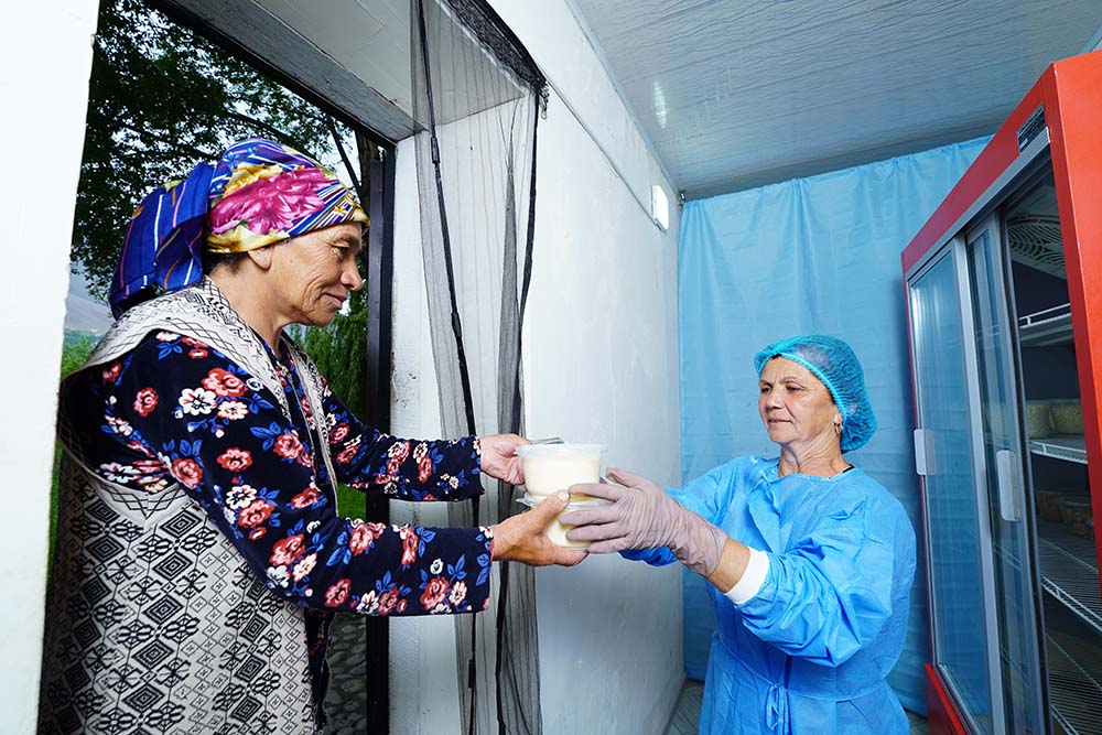 A woman in protective sterilization clothing hands dairy products from a refrigerator to a customer.