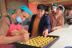 A man pipes pastries onto a tray while three others look on.