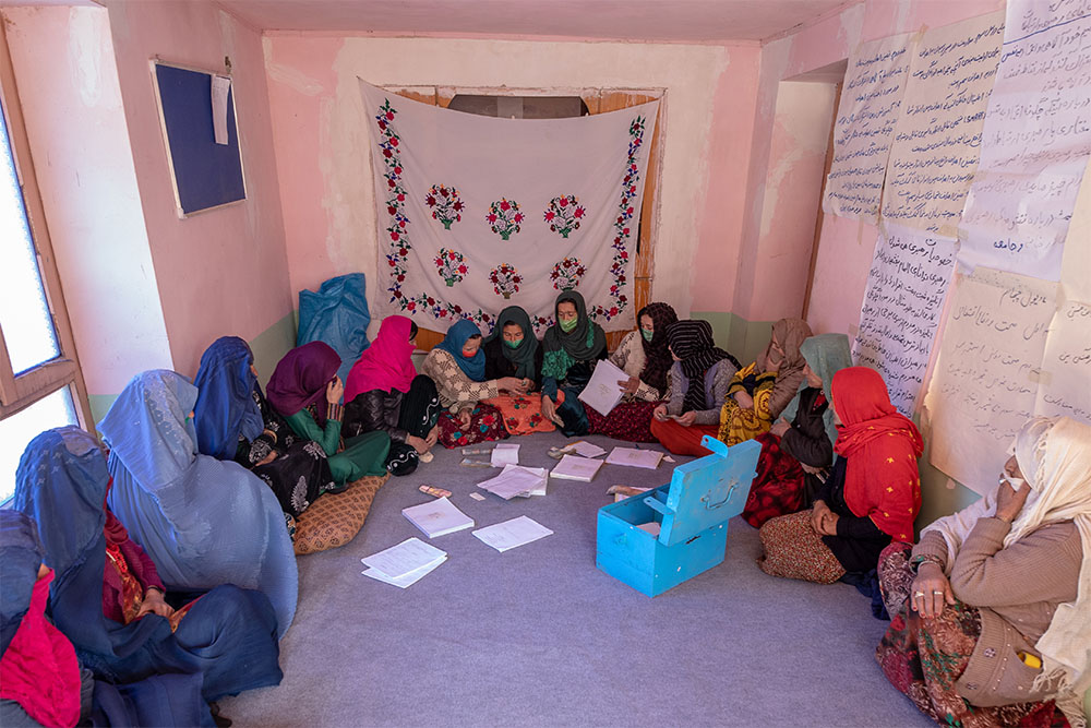 A group of women in Afghanistan look through paperwork to administer their Community-based Savings Group.